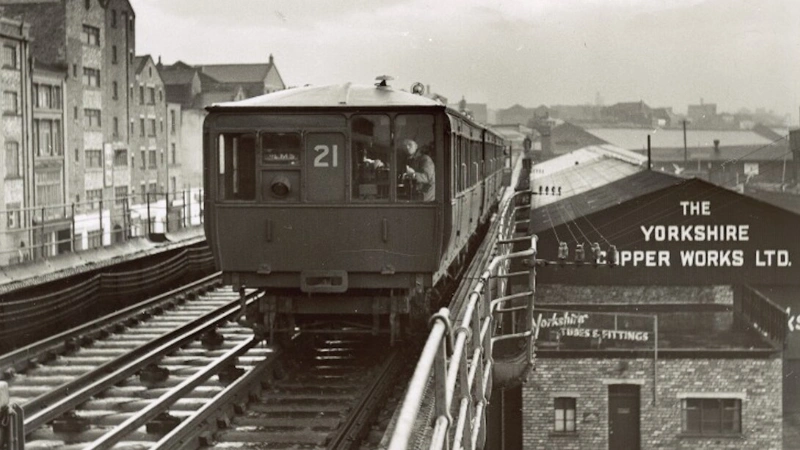 A Liverpool Overhead Railway train on the elevated track above the docks, the Yorkshire Copper Works behind it.